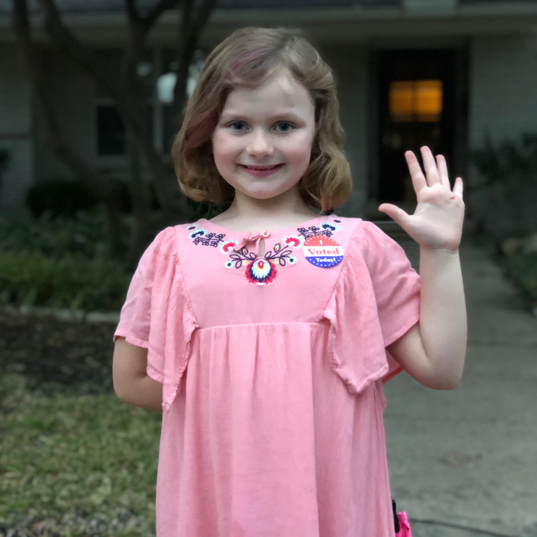 Perry Kate in a pink dress, waving and wearing an I Voted sticker in 2016.