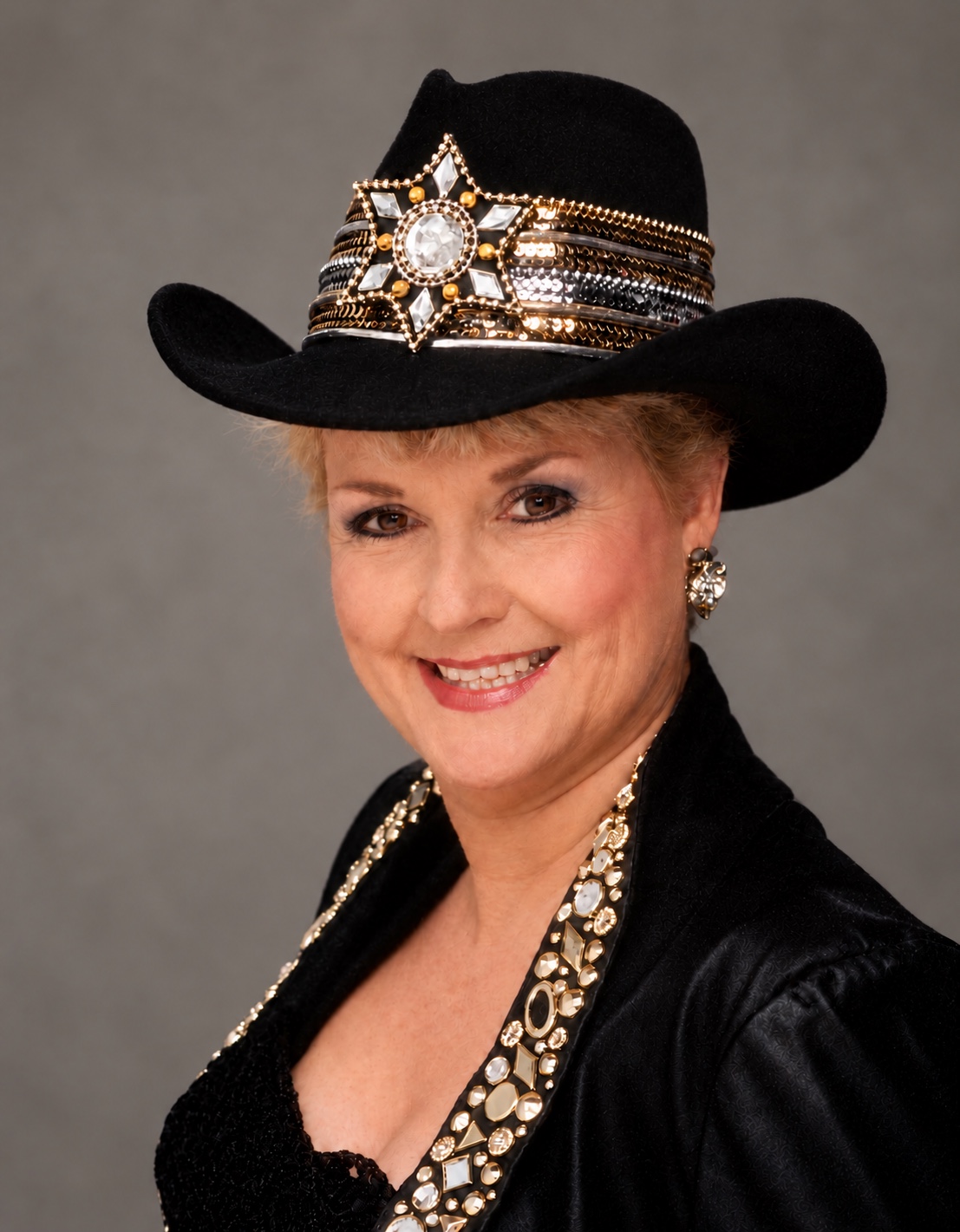 Barbara Gayle Perry Hansen wearing a black cowboy hat with a jeweled band against a neutral gray background