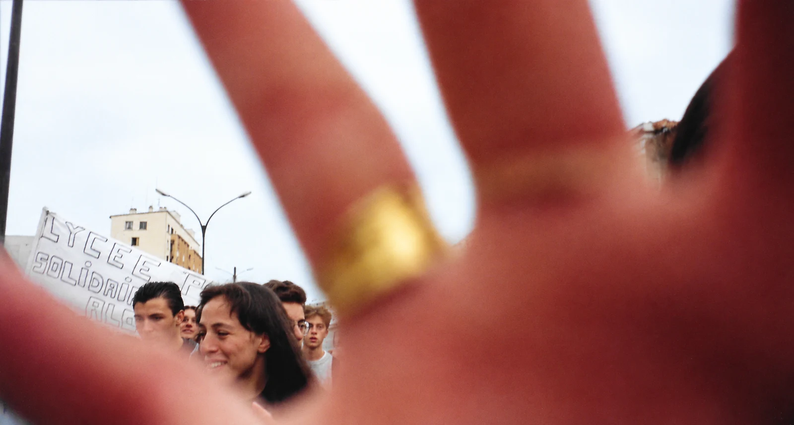 A hand held close to the camera with student protesters behind it in Nîmes, 1998