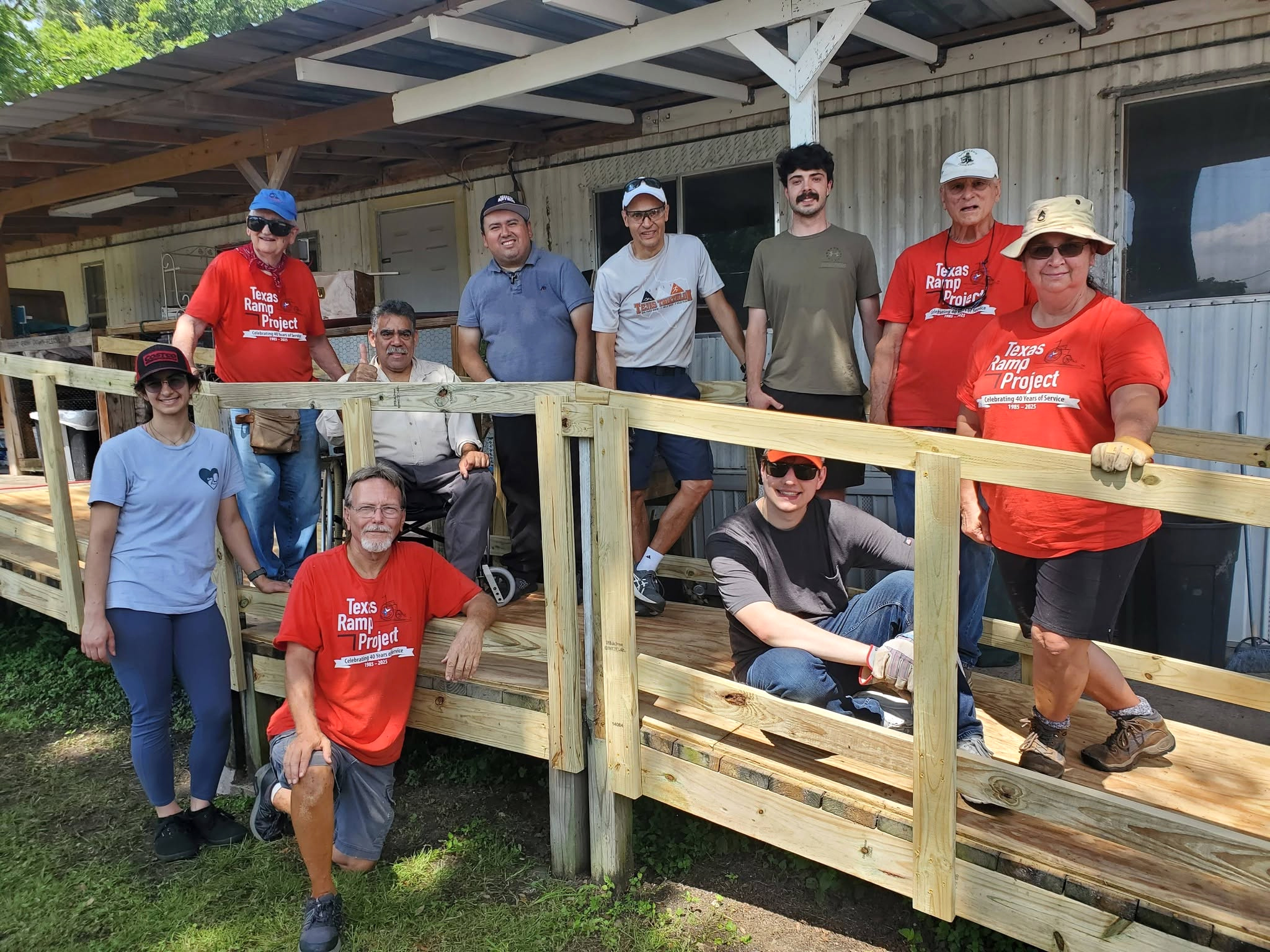 Texas Ramp Project volunteers and a wheelchair user gather on and beside a completed wooden ramp outside a home.